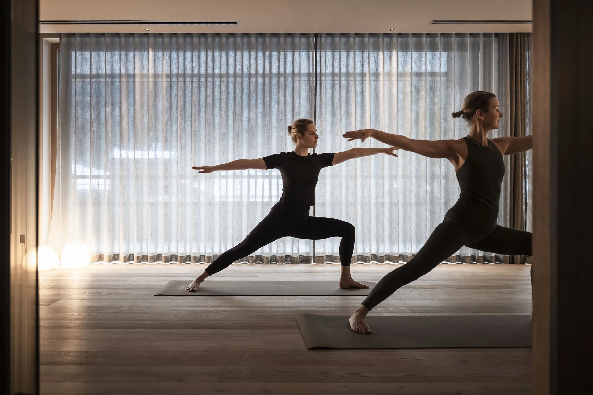 Hotel Monika in Sexten: Wohlbefinden inmitten der Dolomiten Zwei Frauen machen Yoga in der Kriegerpose in einem Raum mit Vorhängen