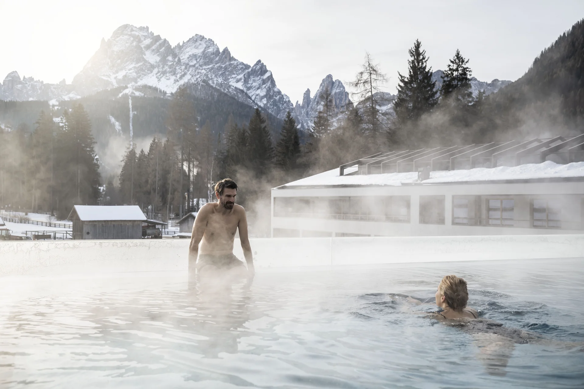 Ihr Hotel an den Drei Zinnen: das Monika in Sexten Zwei Personen im Außenpool mit dampfendem Wasser vor schneebedeckten Bergen