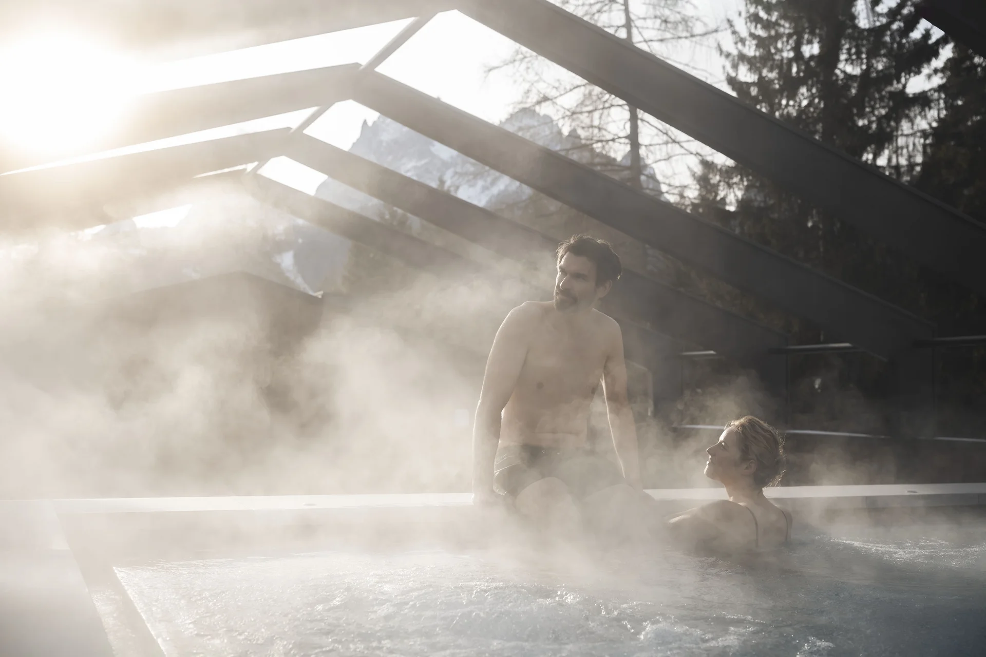 Hotel Monika in Sexten: Wohlbefinden inmitten der Dolomiten Mann und Frau entspannen in dampfendem Außenwhirlpool bei Sonnenuntergang