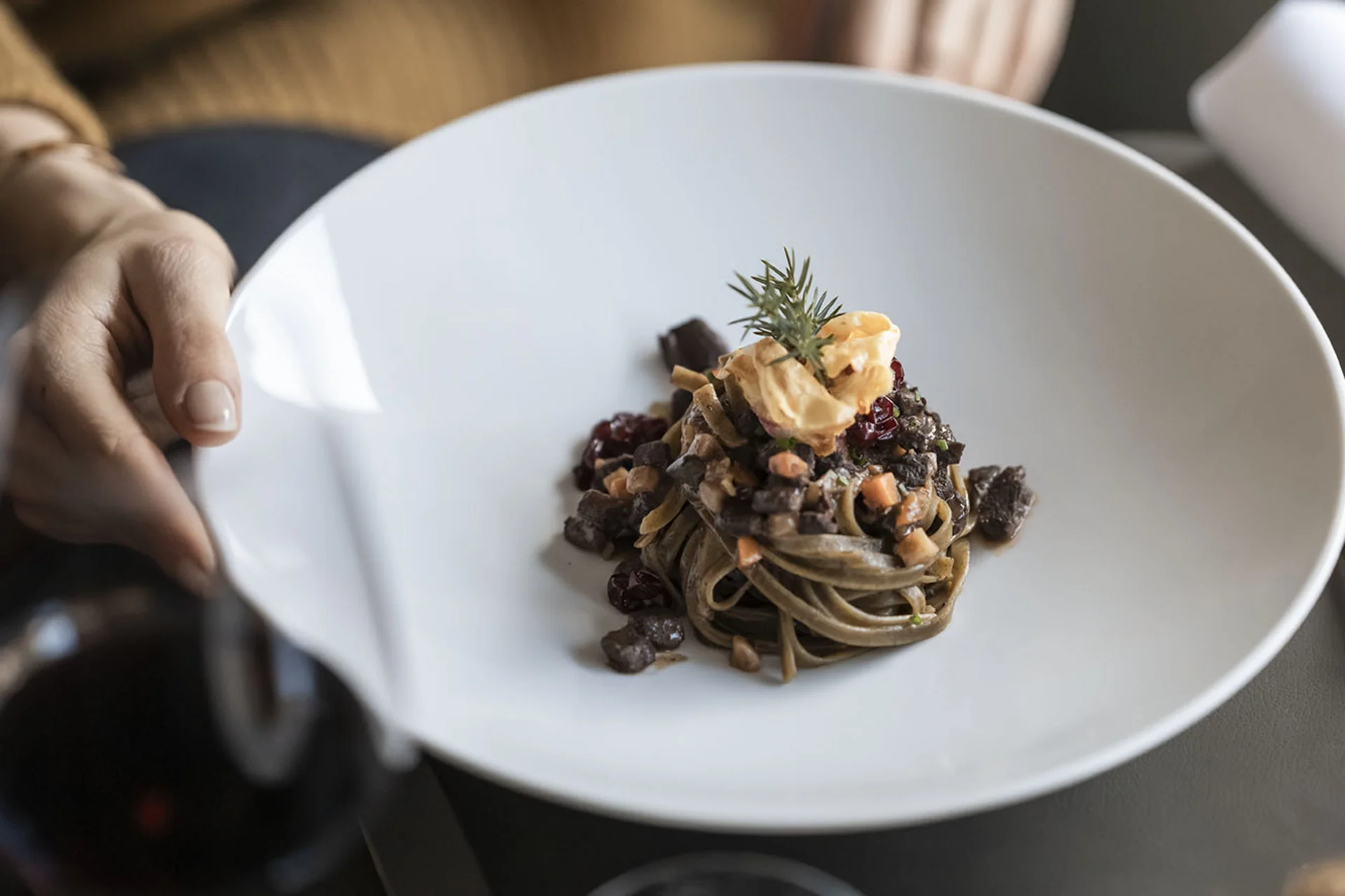 Hotel Monika in Sexten: Wohlbefinden inmitten der Dolomiten Person hält einen weißen Teller mit einer kleinen Portion dekorierter Pasta