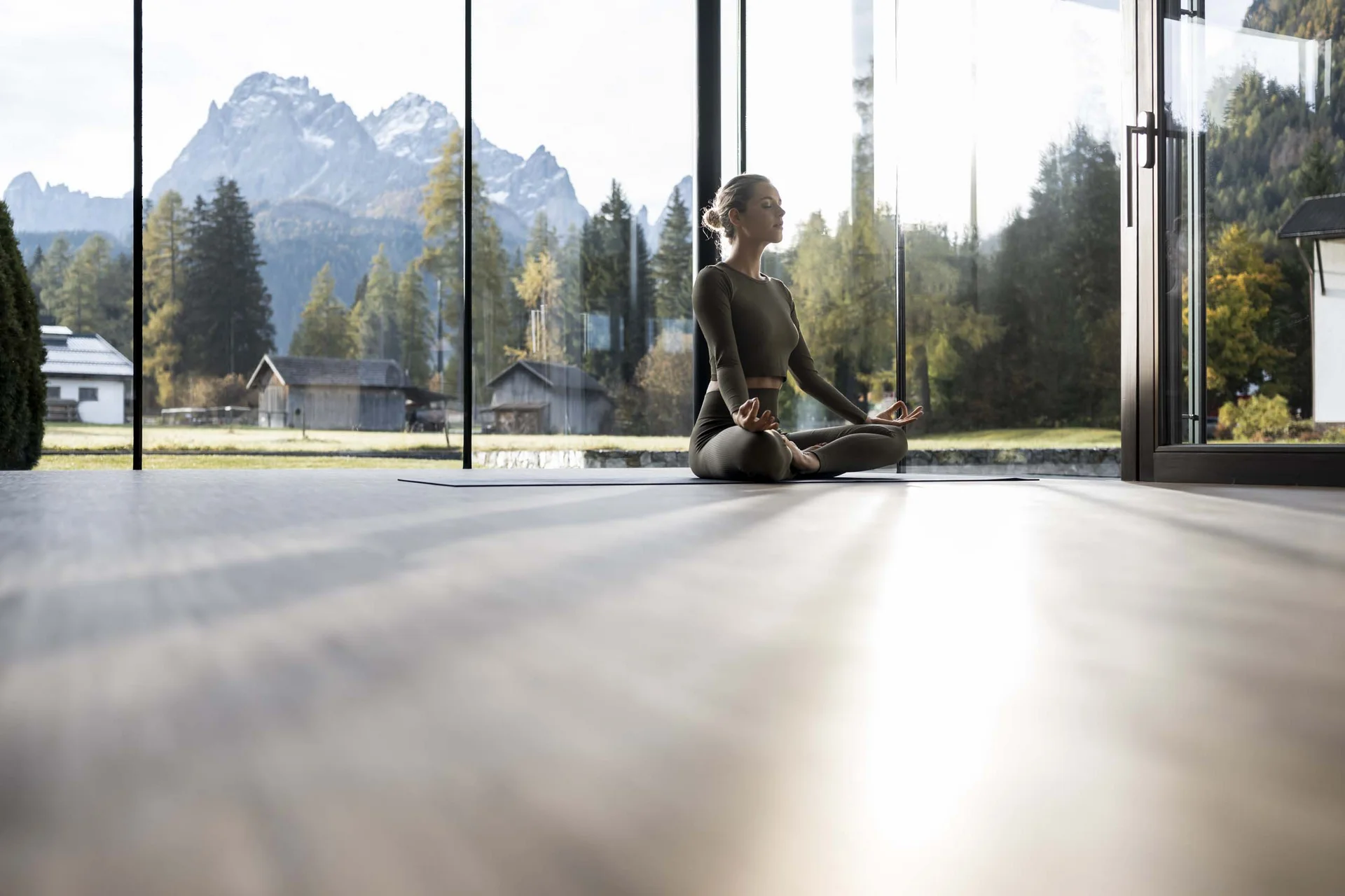Hotel Monika in Sexten: Wohlbefinden inmitten der Dolomiten Frau meditiert drinnen vor Panoramafenstern mit Bergblick