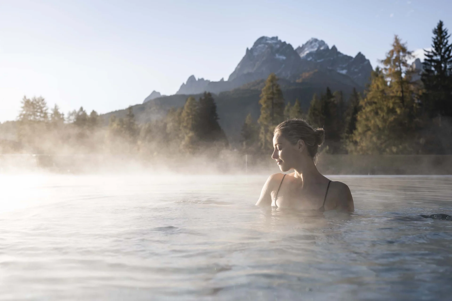 Hotel Monika in Sexten: Wohlbefinden inmitten der Dolomiten Frau entspannt im heißen Thermalbad mit Bergpanorama im Hintergrund
