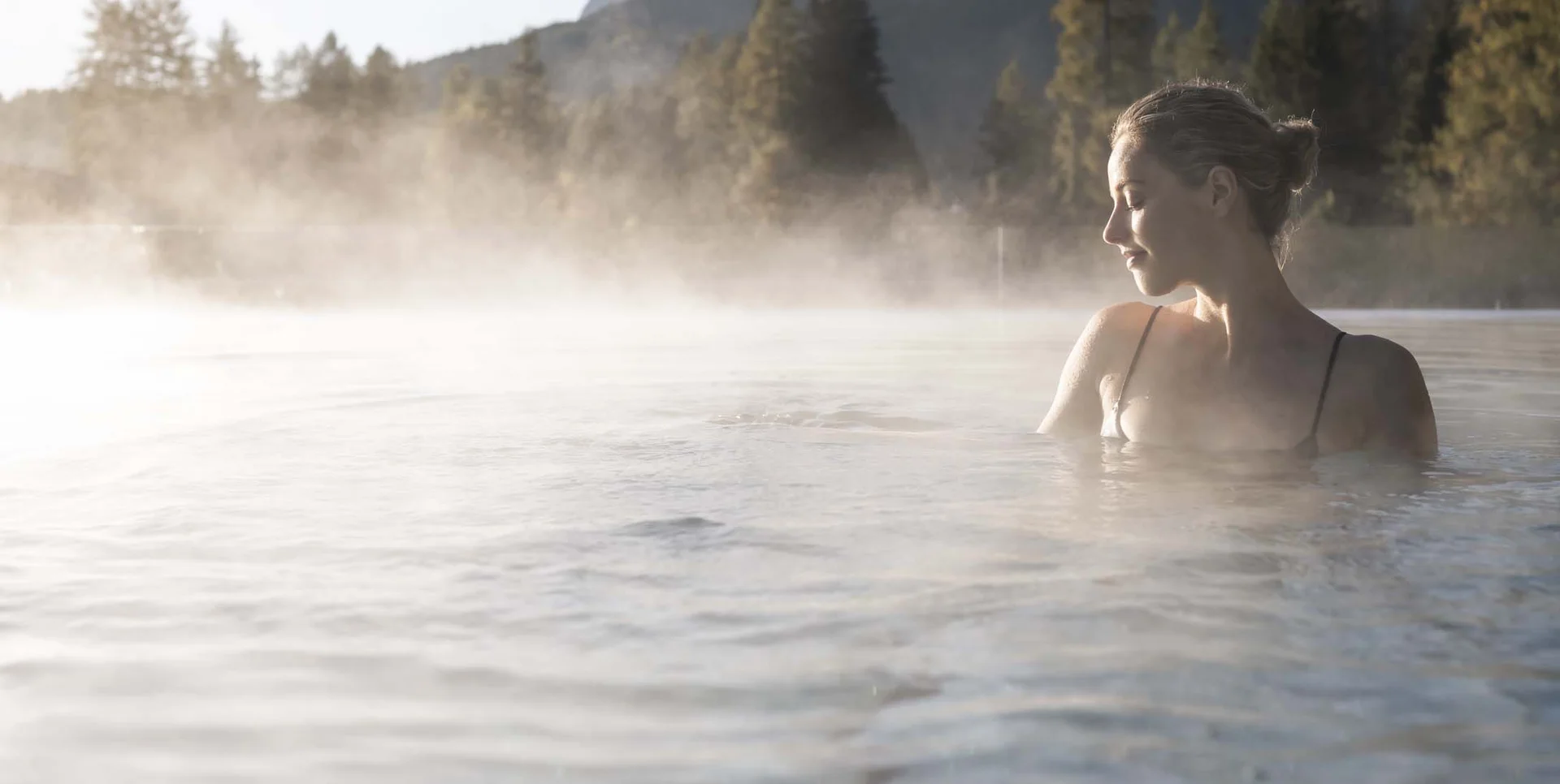 A new dimension of well-being: your wellness hotel in Sexten Woman relaxing in hot spring pool with mountain scenery in background
