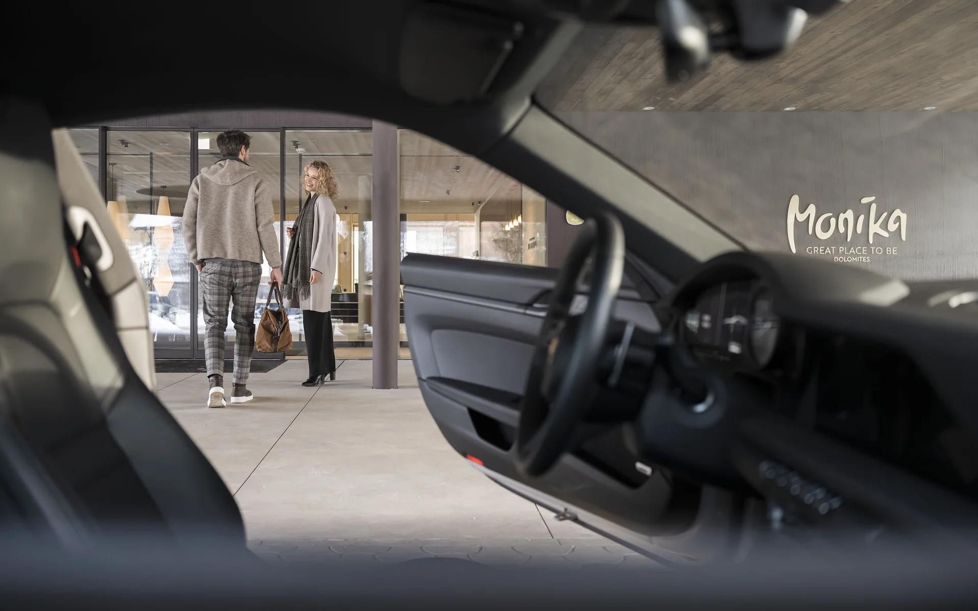 Das Hideaway für Ihren luxuriösen Urlaub im Pustertal Blick durch ein Auto auf zwei Menschen vor einem Gebäude mit Monika-Logo