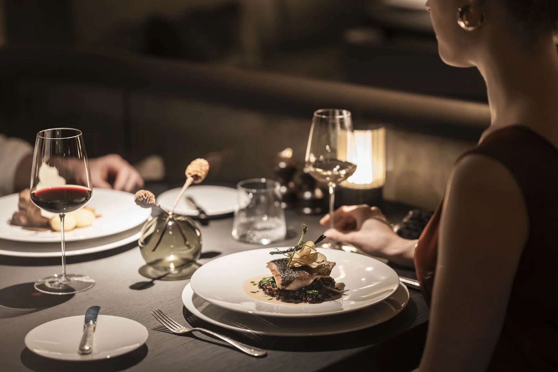 À-la-carte-Restaurant CANA in Sexten Elegantes Abendessen mit Weingläsern und serviertem Gourmetgericht