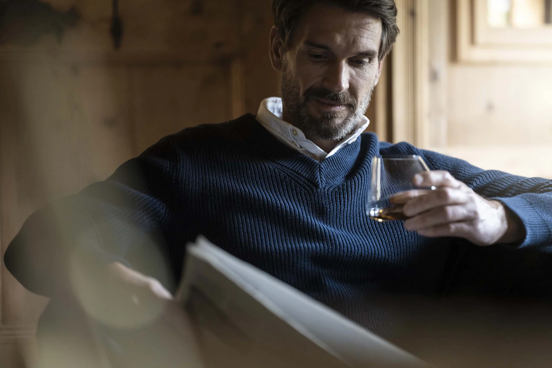Hotel Monika in Sexten: Wohlbefinden inmitten der Dolomiten Mann in blauem Pullover liest Zeitung und hält ein Glas Whisky