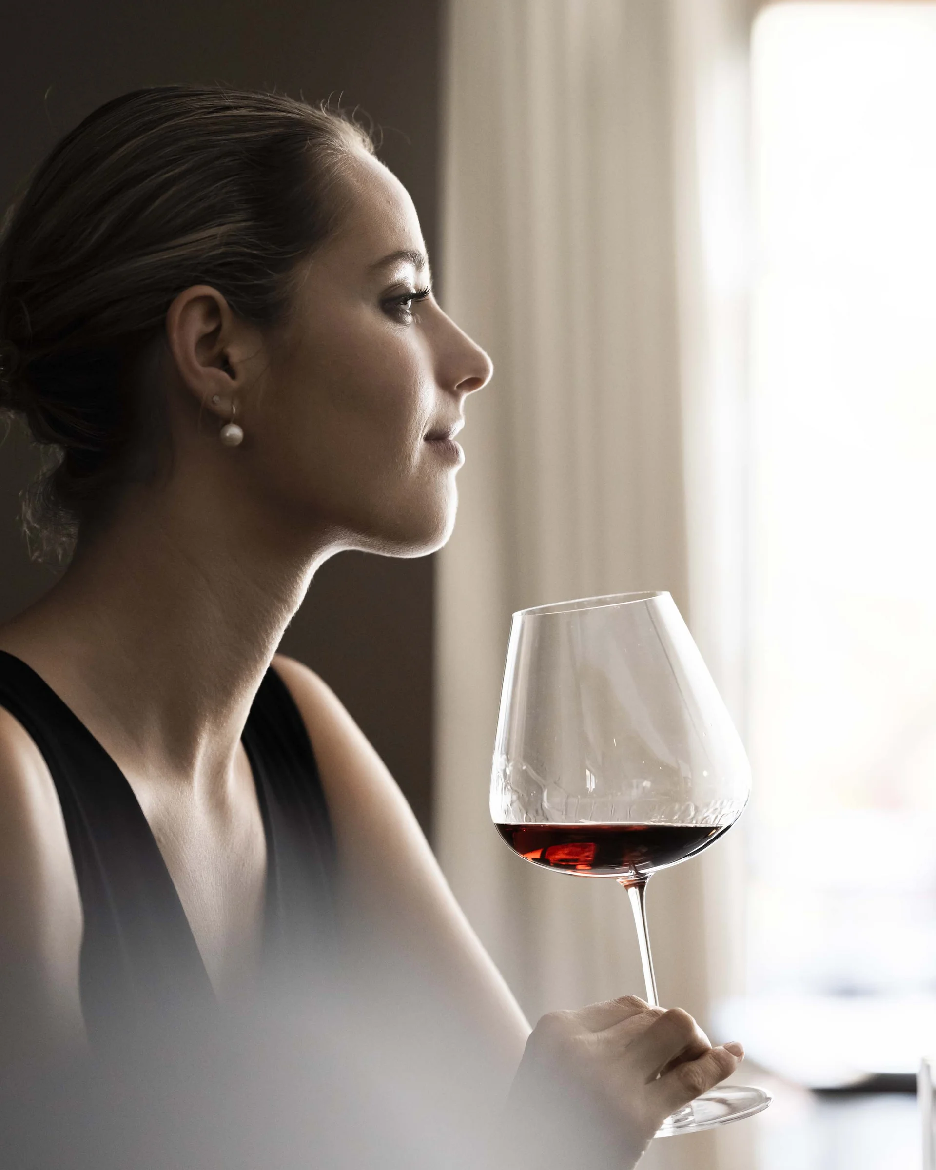 A new dimension of taste: your gourmet hotel in South Tyrol. Elegant woman holding a glass of red wine looking out the window
