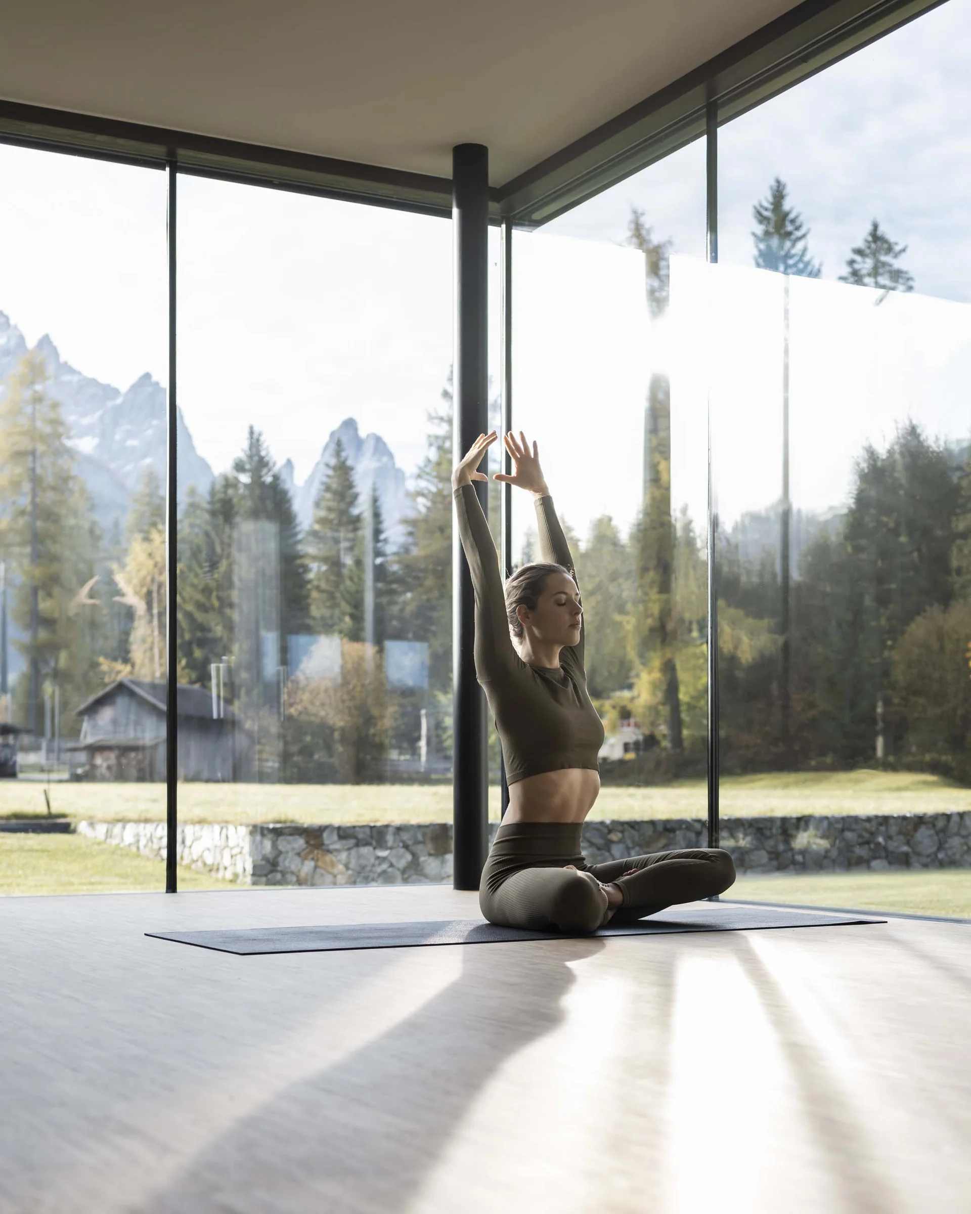 Hotel Monika in Sexten: Wohlbefinden inmitten der Dolomiten Frau macht Yoga im modernen Raum mit Bergblick durch große Fenster