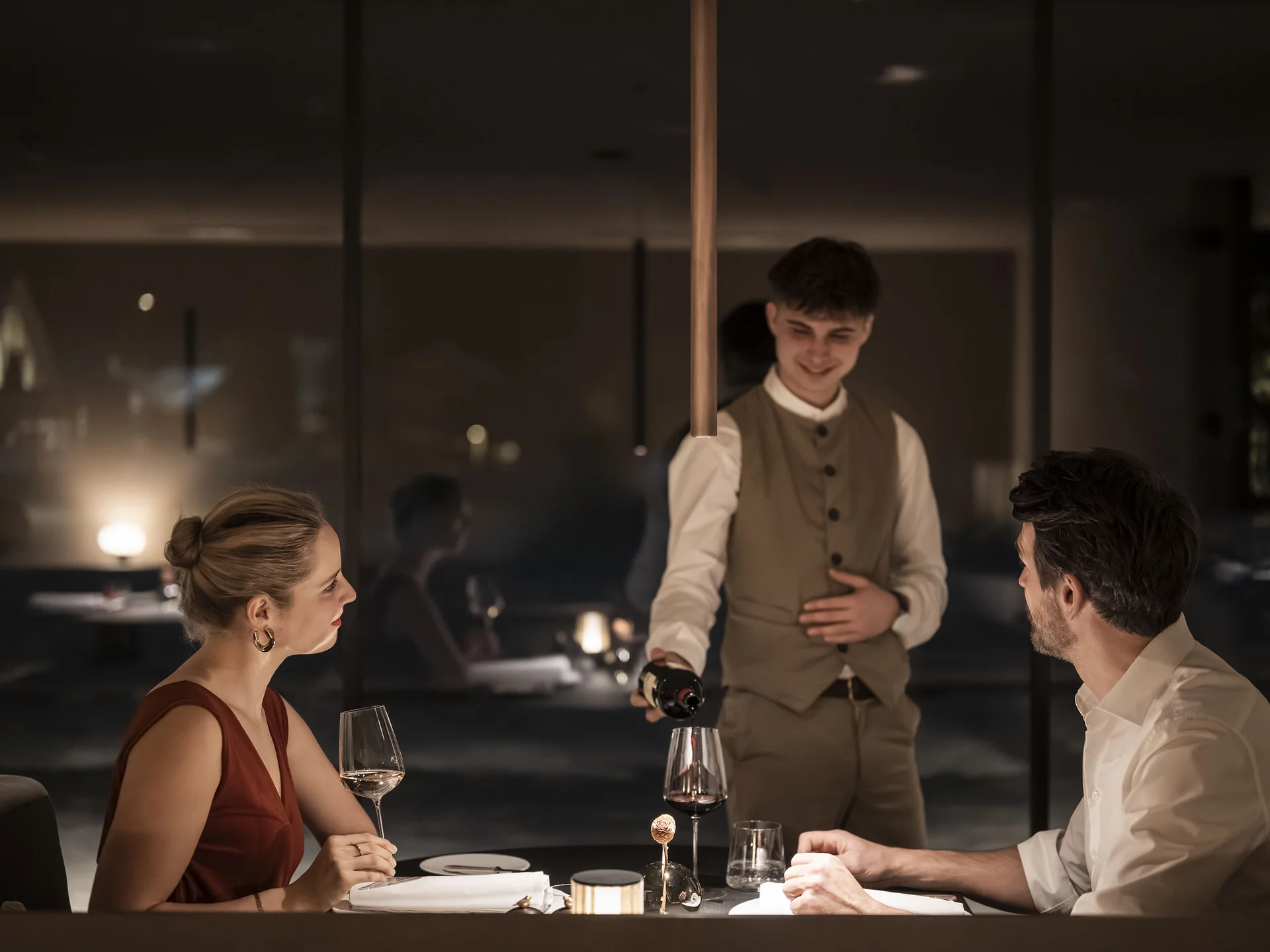 À-la-carte-Restaurant CANA in Sexten Kellner schenkt Wein ein zu einem romantischen Abendessen im Restaurant