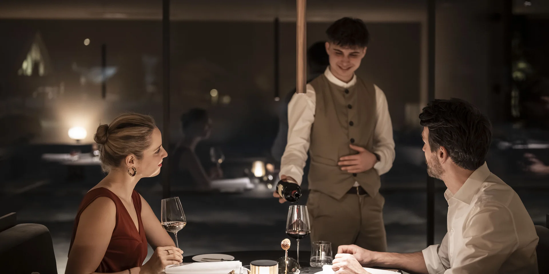 Genuss in neuer Dimension: Ihr Gourmethotel in Südtirol Kellner schenkt Wein ein zu einem romantischen Abendessen im Restaurant