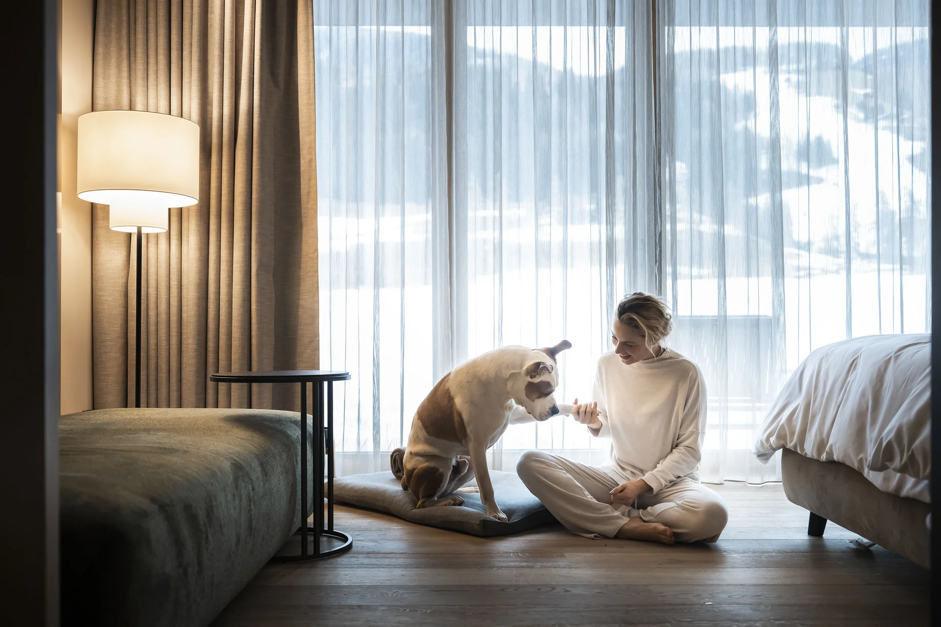 Das Wellnesshotel für den Urlaub mit Hund in Südtirol Frau gibt Hund Pfote sitzend auf Boden vor Fenster mit Vorhängen