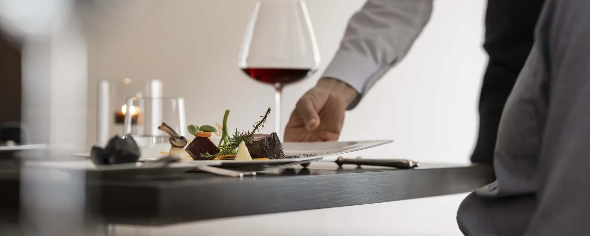 CANA à la carte restaurant in Sexten Waiter serving gourmet dish with red wine at restaurant table