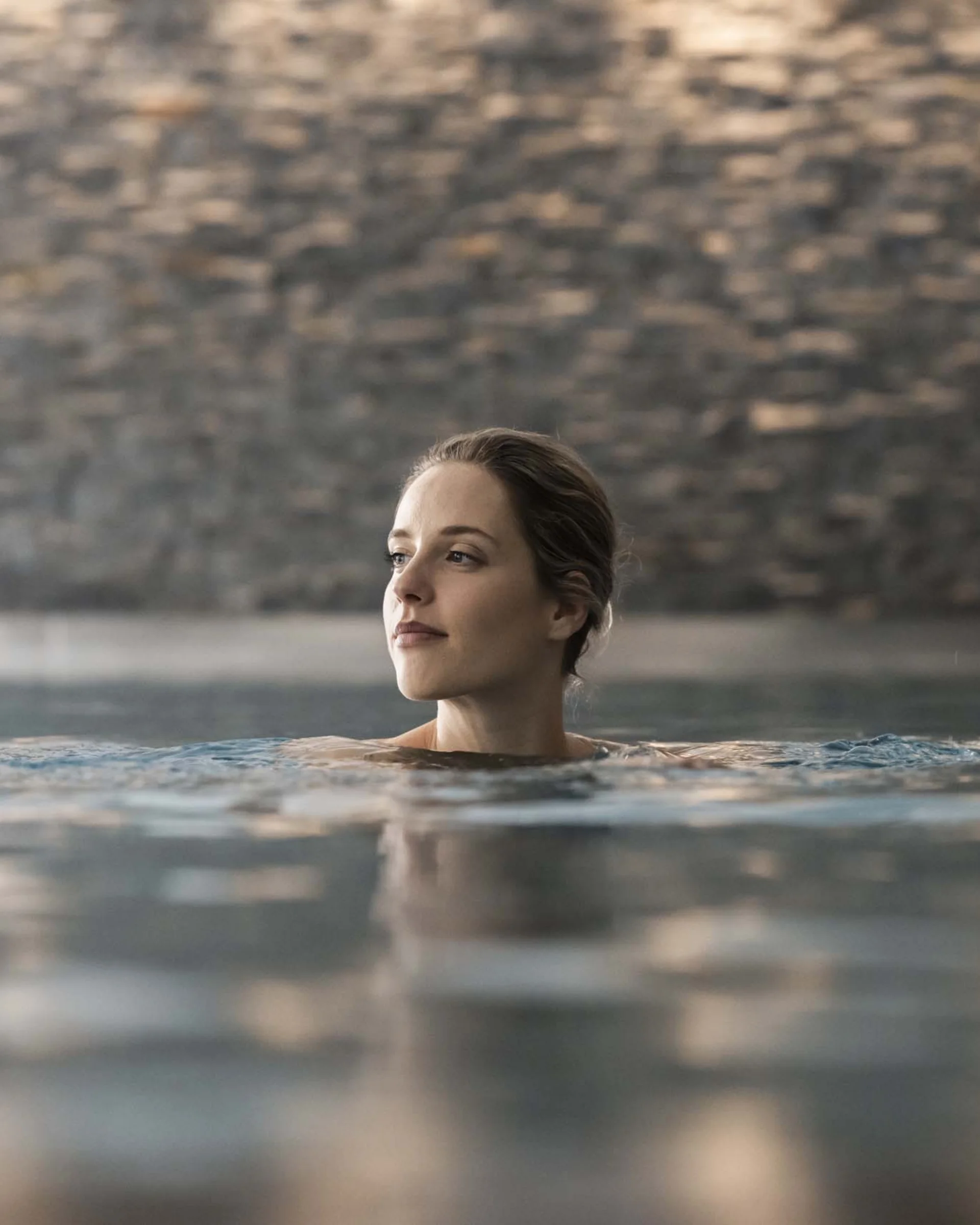 A new dimension of well-being: your wellness hotel in Sexten Woman relaxing in indoor pool with blurred stone wall background