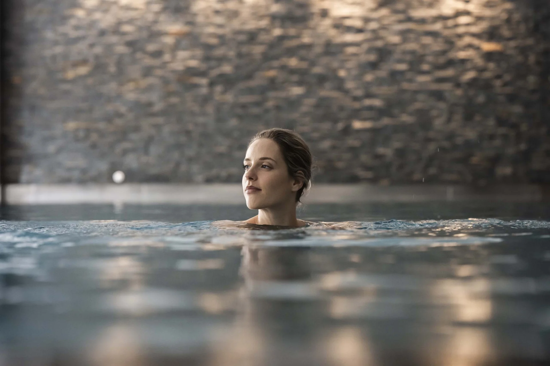 Hotel Monika in Sexten: Wohlbefinden inmitten der Dolomiten Frau entspannt im Hallenbad mit unscharfem Hintergrund aus Steinen