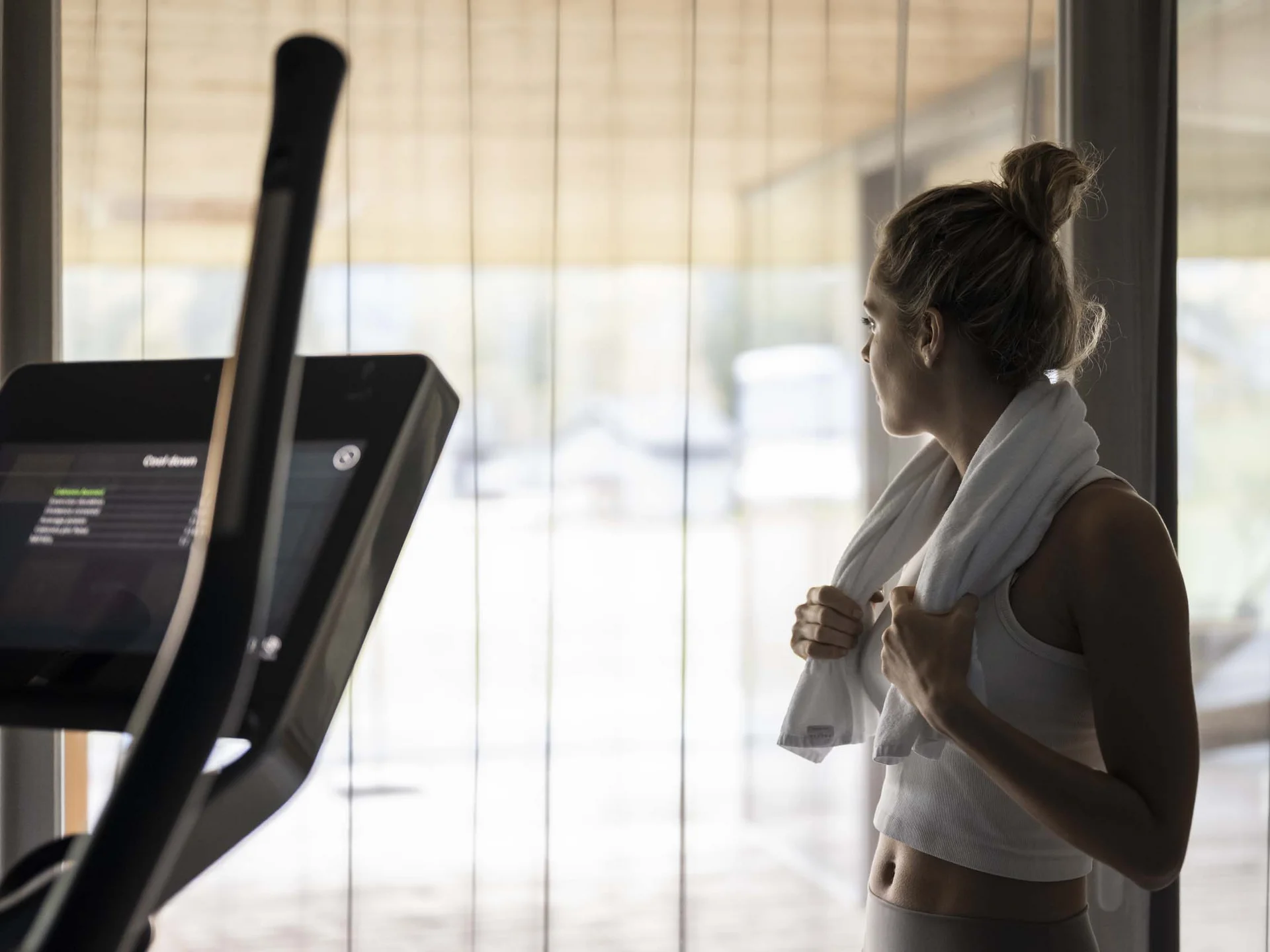 Fitness, yoga, outdoor fun: active hotel in South Tyrol. Woman in gym with towel around neck looking out the window