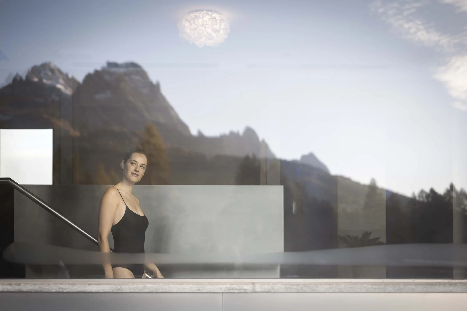 Hotel Monika in Sexten: Wohlbefinden inmitten der Dolomiten Frau im schwarzen Badeanzug in einem modernen Pool mit Bergblick