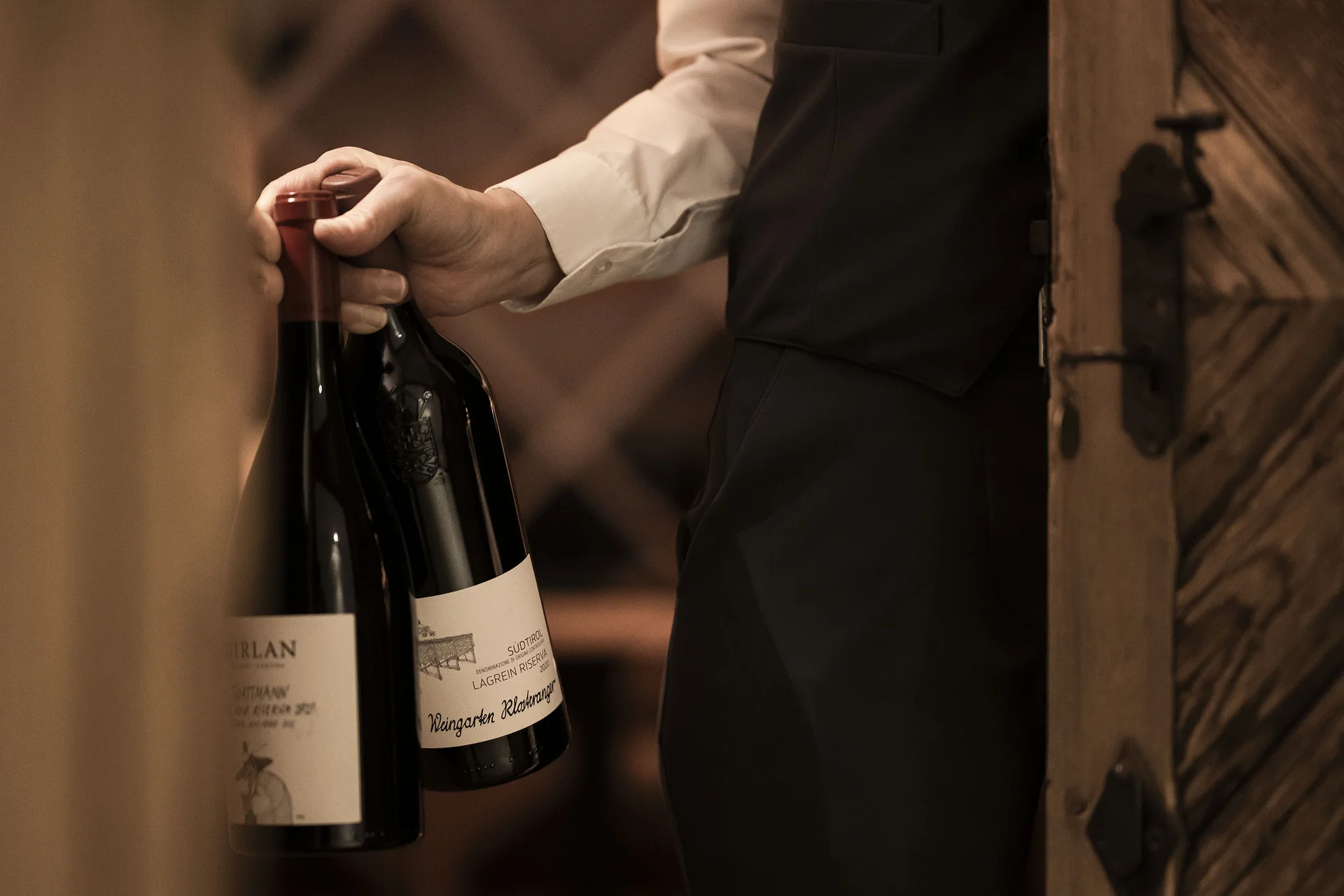 À-la-carte-Restaurant CANA in Sexten Mann trägt zwei Flaschen Wein in einem Weinkeller