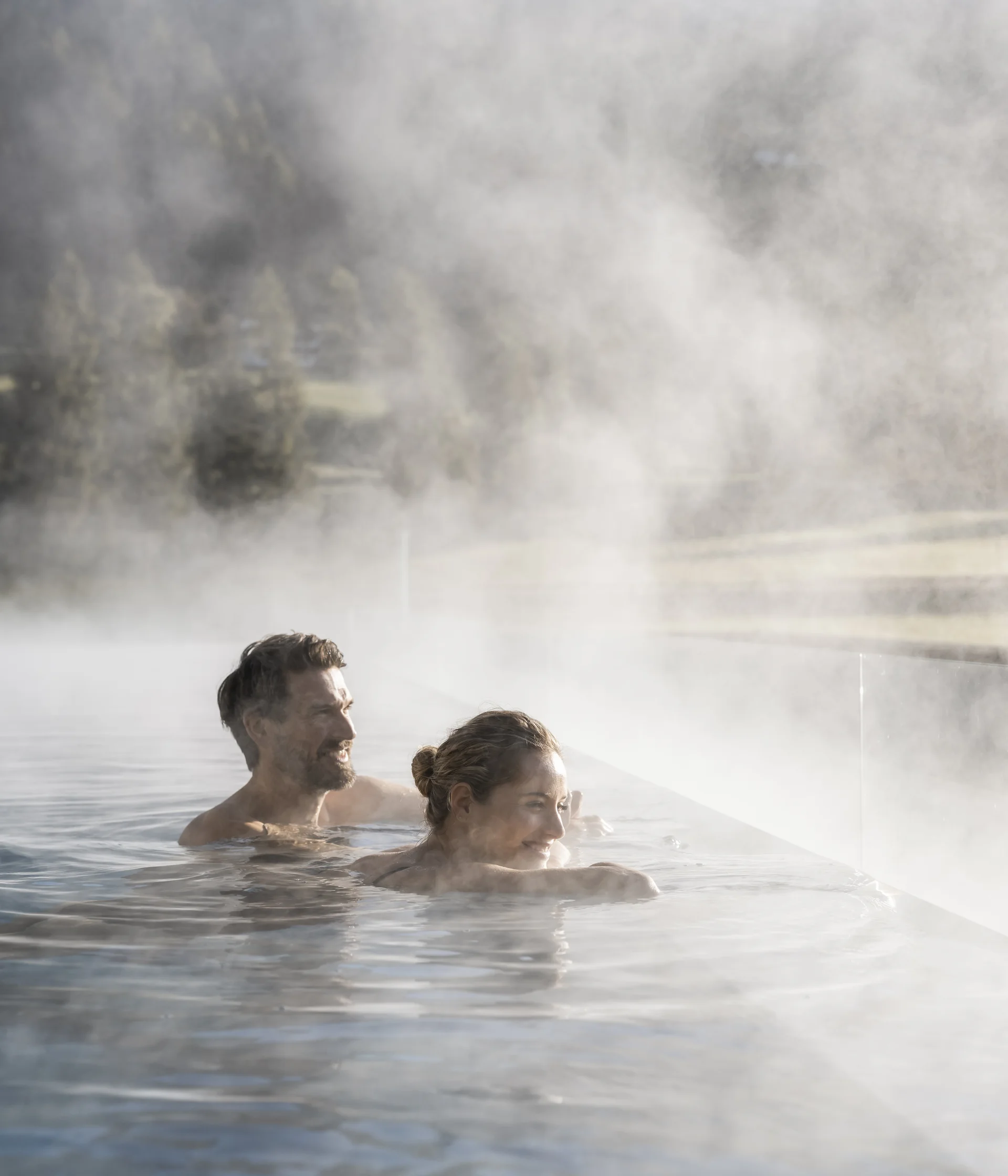 Wohlbefinden in neuer Dimension: Ihr Wellnesshotel in Sexten Mann und Frau entspannen im dampfenden Außenpool mit Bergblick
