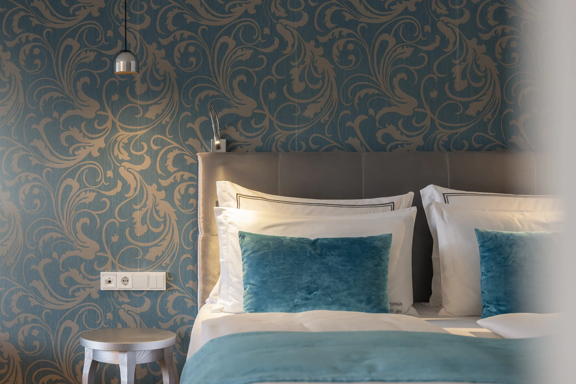 Hotel Monika in Sexten: Wohlbefinden inmitten der Dolomiten Nahaufnahme von Betten mit blauen Kissen und gemusterten Tapeten im Zimmer