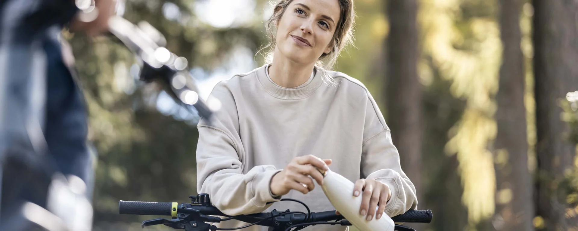 Fitness, yoga, outdoor fun: active hotel in South Tyrol. Woman with bicycle drinking from bottle in forest daylight