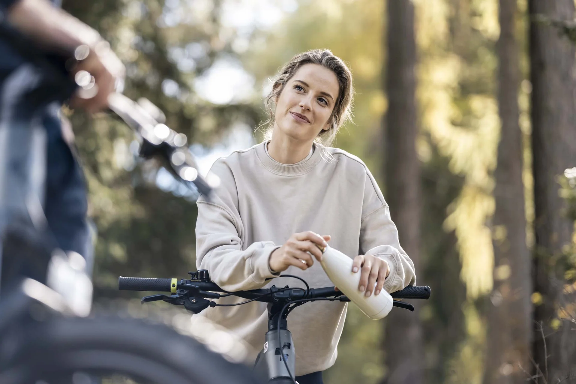 Fitness, yoga, outdoor fun: active hotel in South Tyrol. Woman with bicycle drinking from bottle in forest daylight