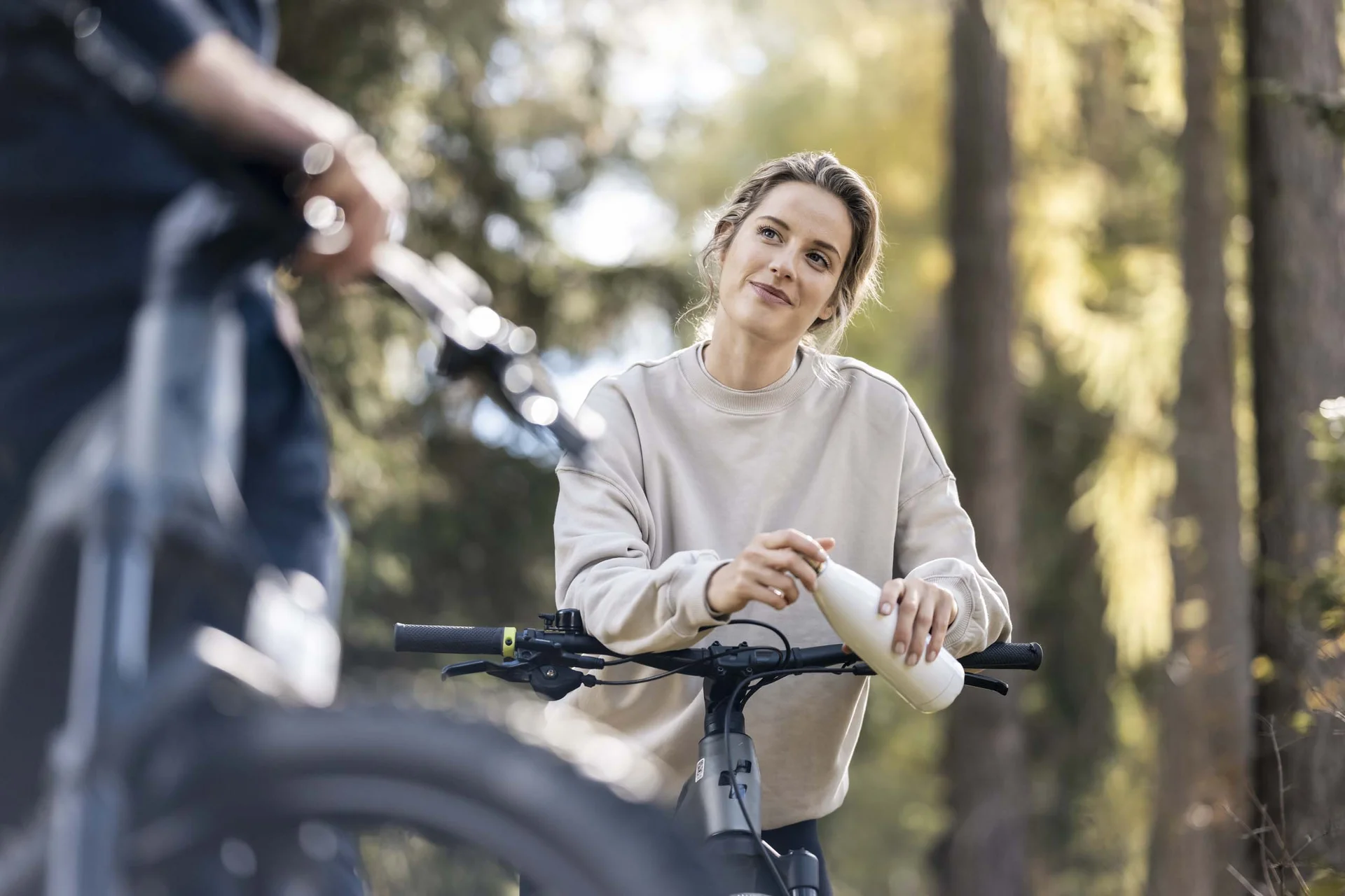 Hotel Monika in Sexten: Wohlbefinden inmitten der Dolomiten Frau mit Fahrrad trinkt aus Flasche im Wald bei Tageslicht