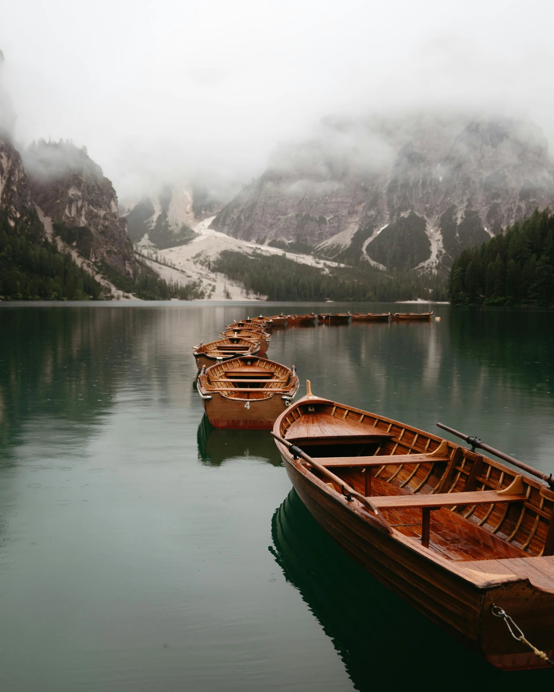 Hotel Monika: a new dimension of luxury Row of wooden boats on lake with foggy mountains in background