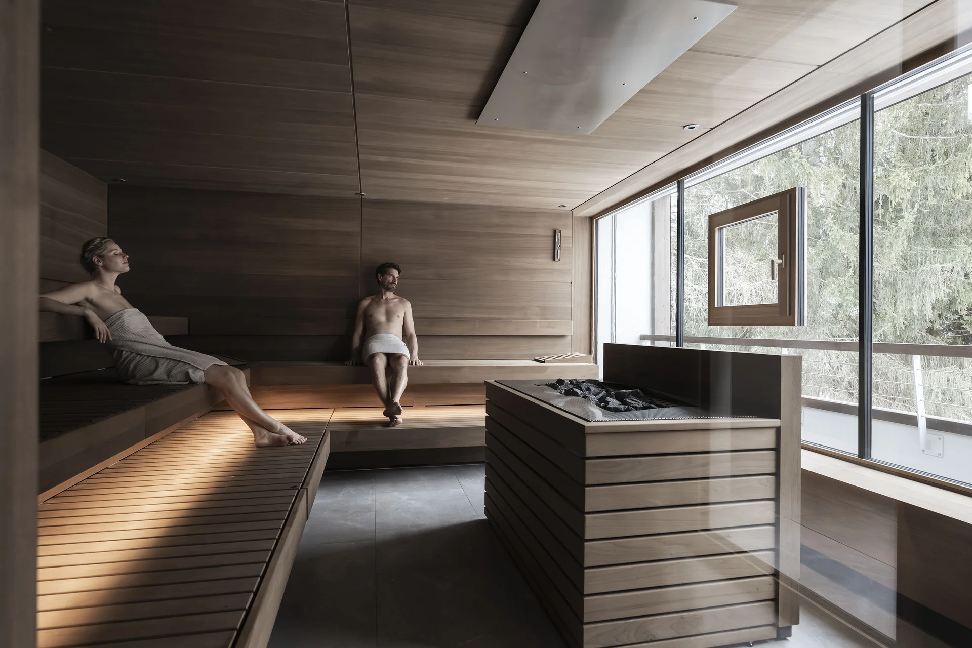 Hotel Monika in Sexten: Wohlbefinden inmitten der Dolomiten Zwei Personen entspannen in einer holzverkleideten Sauna mit Blick ins Freie