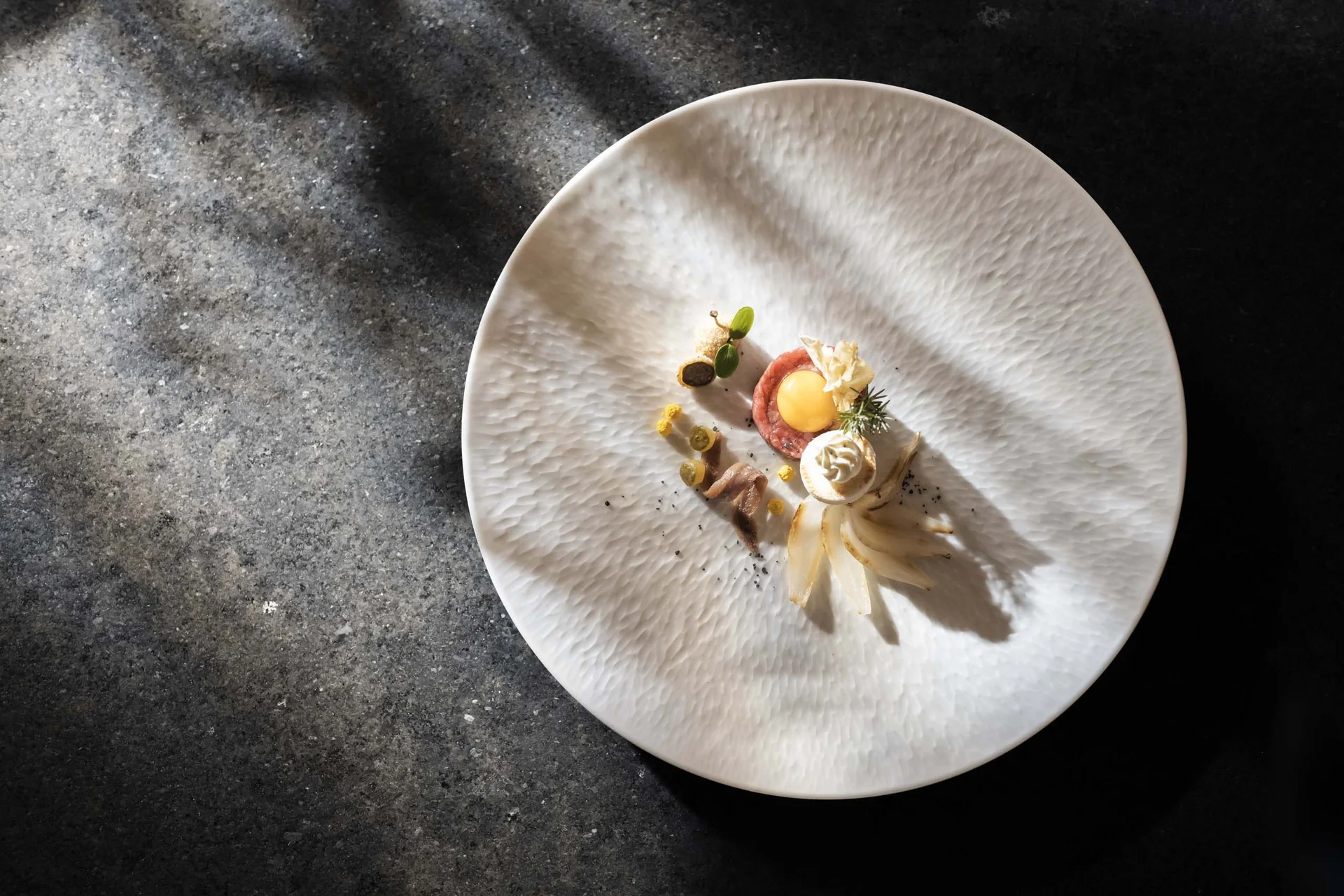 Hotel Monika in Sexten: Wohlbefinden inmitten der Dolomiten Fein angerichtetes Gericht auf weißem Teller mit dunklem Hintergrund