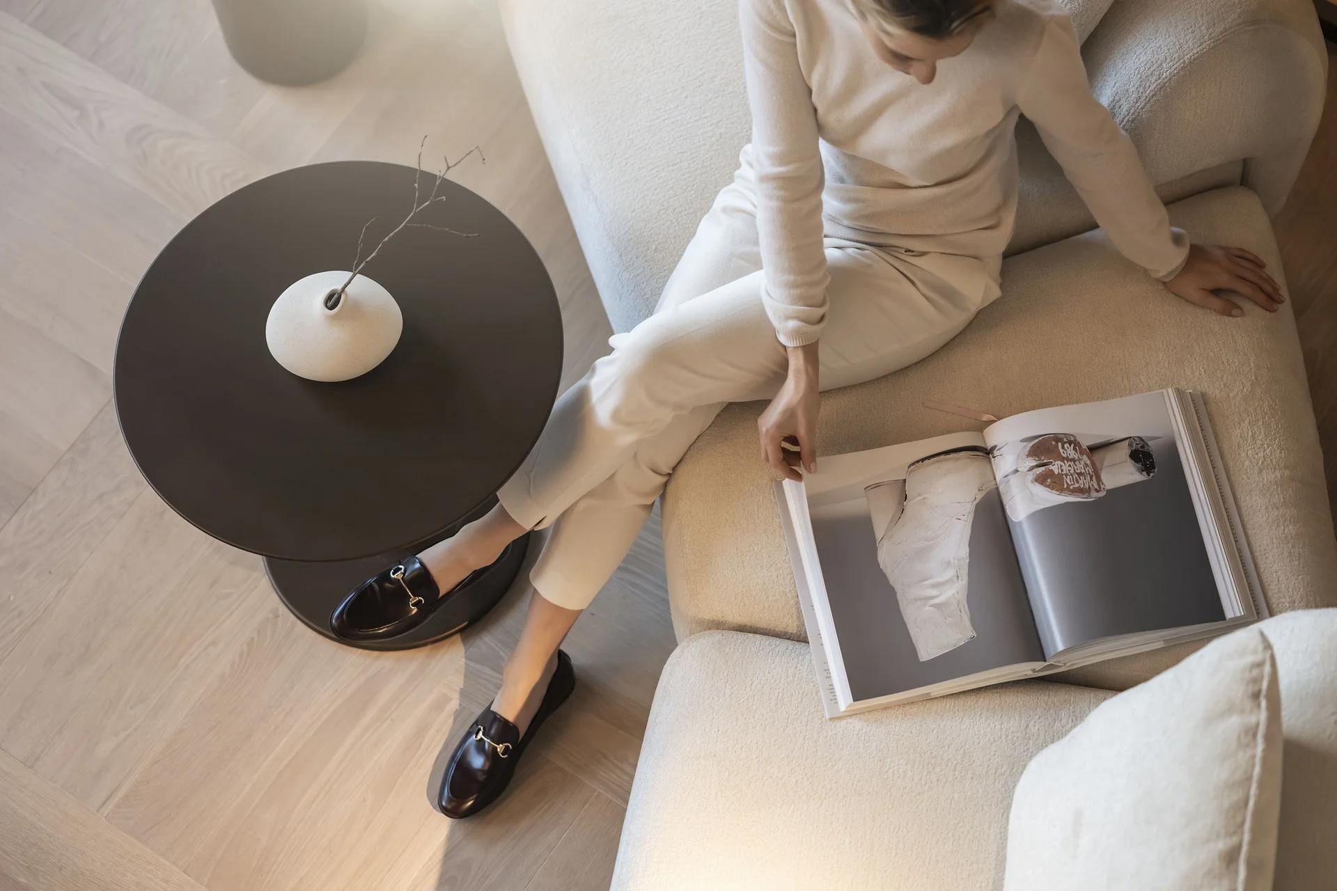 Hotel Monika in Sexten: Wohlbefinden inmitten der Dolomiten Frau sitzt auf Sofa und blättert in einem Magazin neben einem Tisch mit Vase