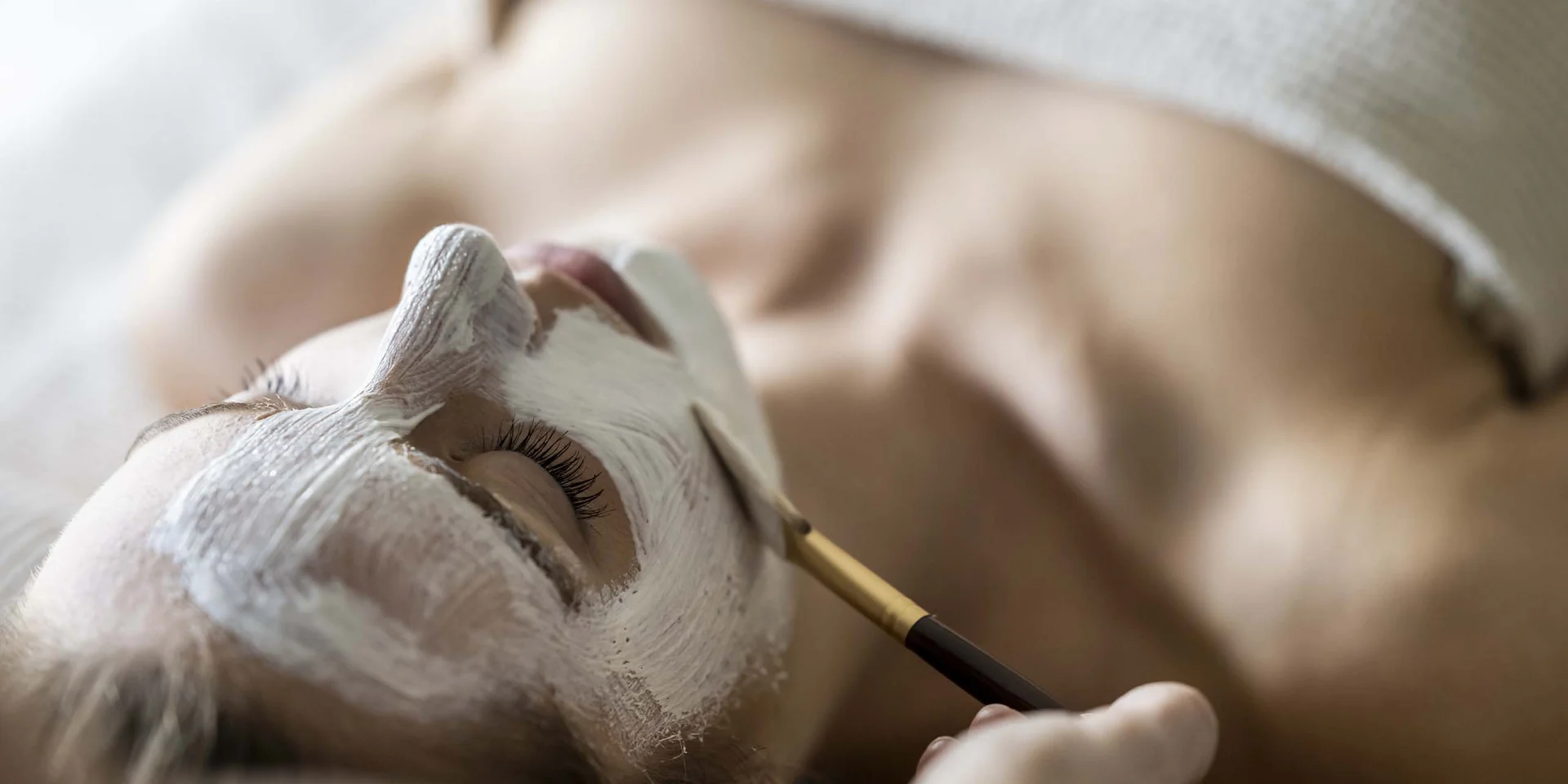 Wohlbefinden in neuer Dimension: Ihr Wellnesshotel in Sexten Frau erhält eine Gesichtsmaske mit Pinsel in einem Wellness-Spa