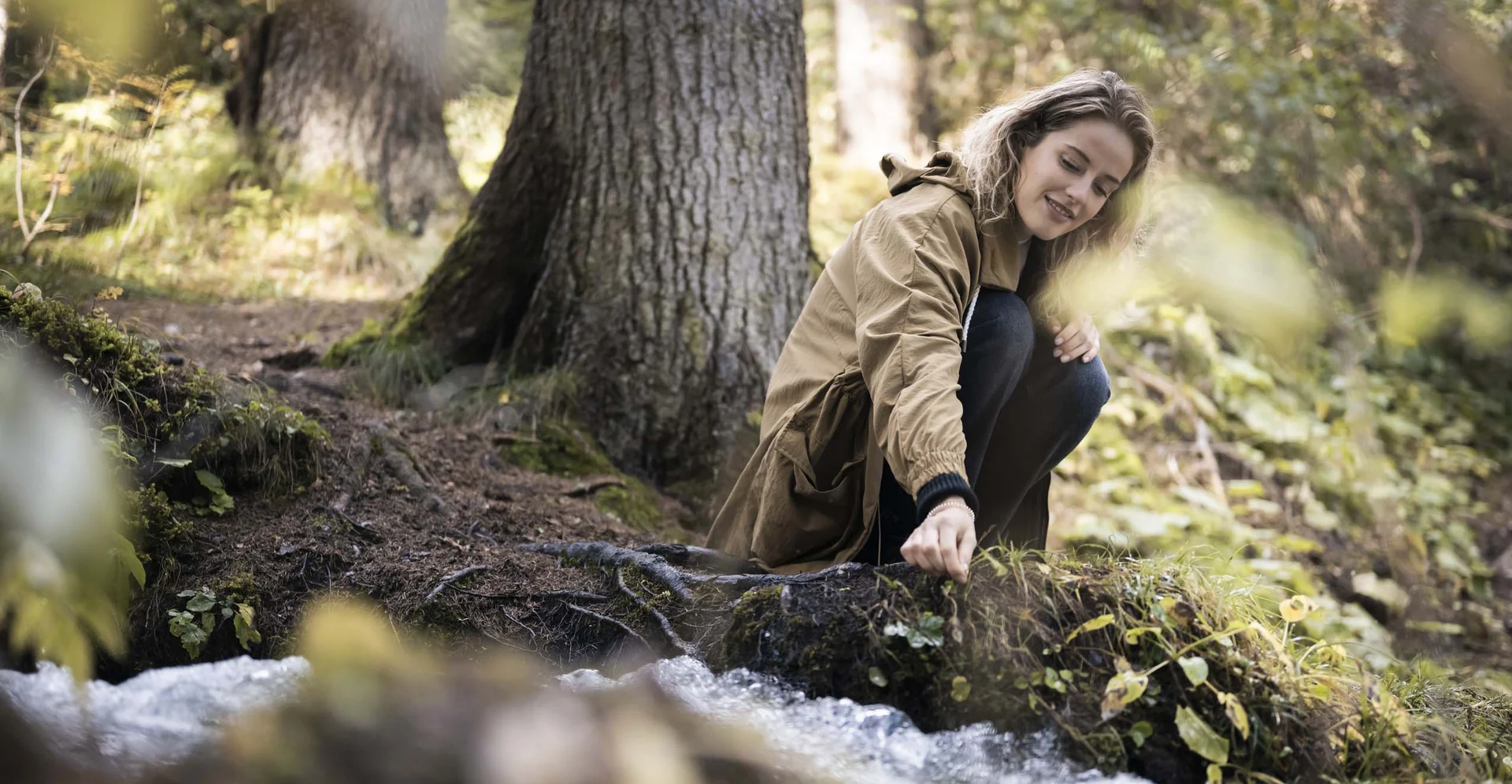 Holiday in and with nature: your adventure hotel in South Tyrol. Woman sitting by the forest touching water of a stream