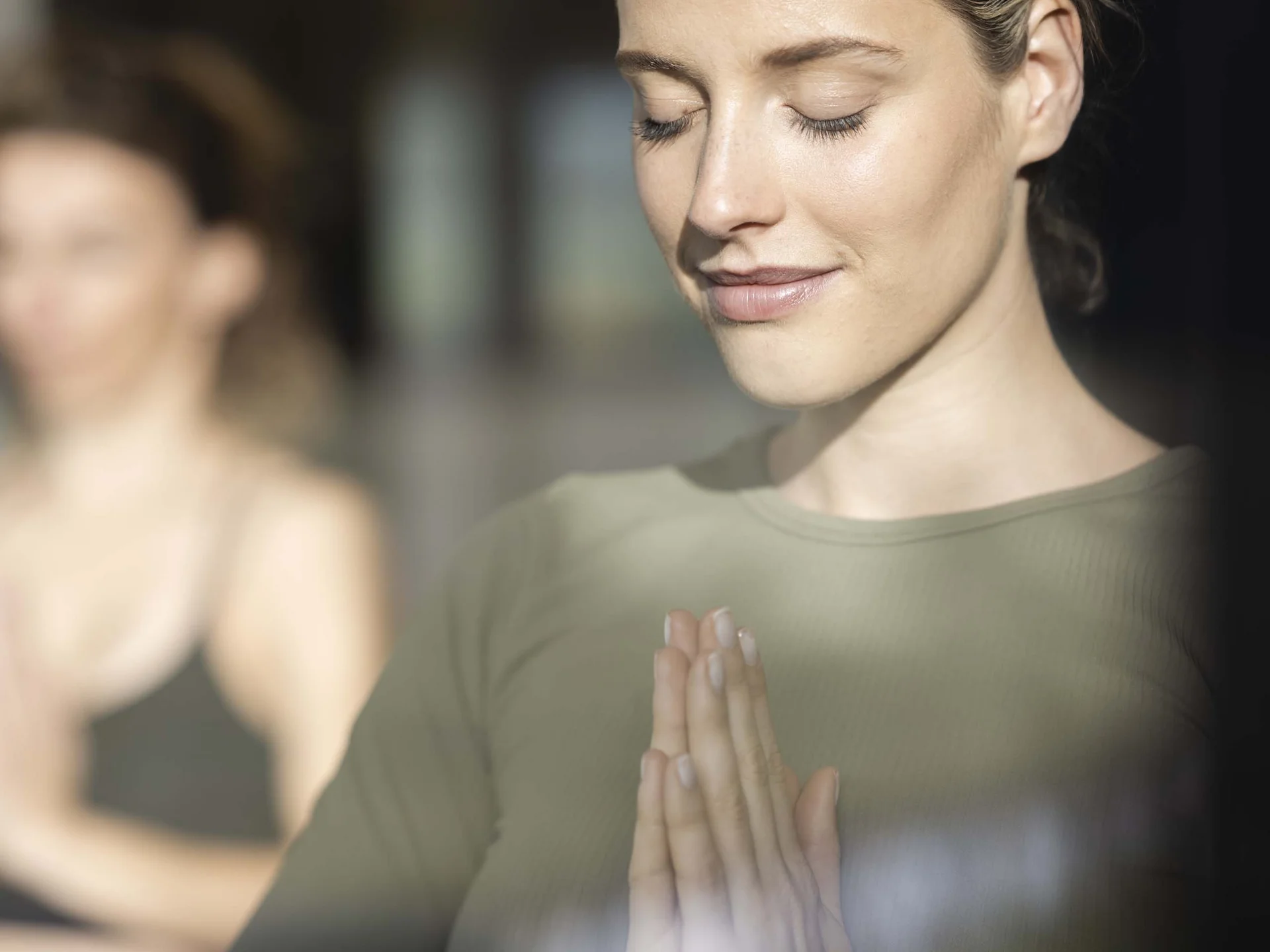 Fitness, yoga, outdoor fun: active hotel in South Tyrol. Woman in green clothing meditating with hands together and eyes closed