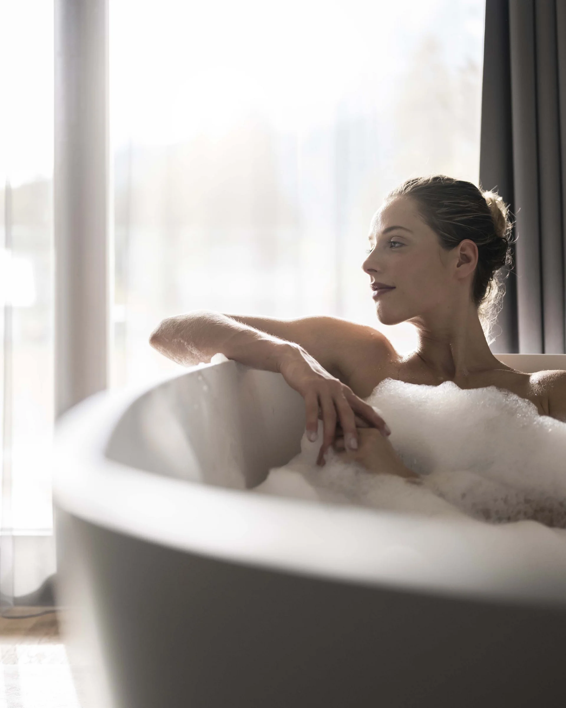 Hotel Monika in Sexten: Wohlbefinden inmitten der Dolomiten Frau entspannt in Badewanne mit Schaum vor hellem Fenster