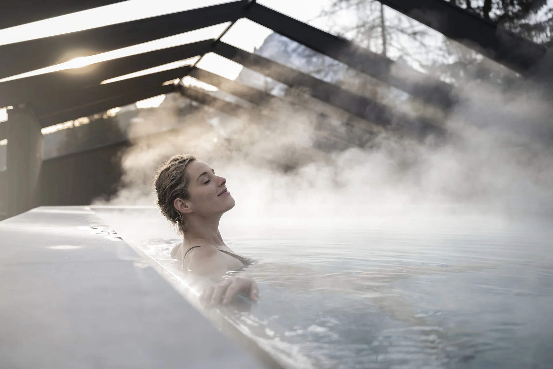 Hotel Monika in den Dolomiten – mit Pools und Spa Area Frau entspannt in dampfendem Thermalbad unter Glasdach