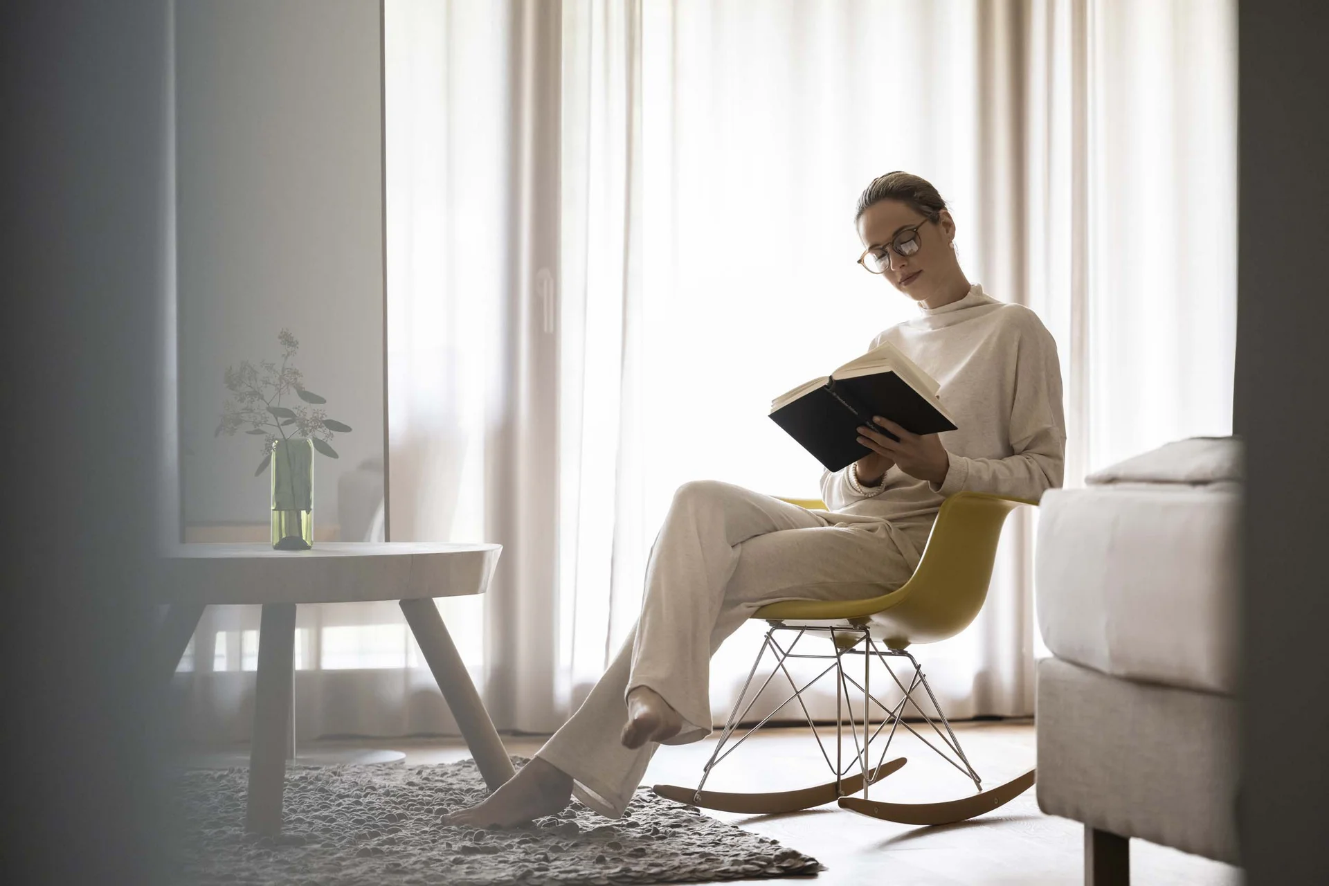 Hotel Monika in Sexten: Wohlbefinden inmitten der Dolomiten Frau liest Buch entspannt auf einem gelben Schaukelstuhl im Wohnzimmer