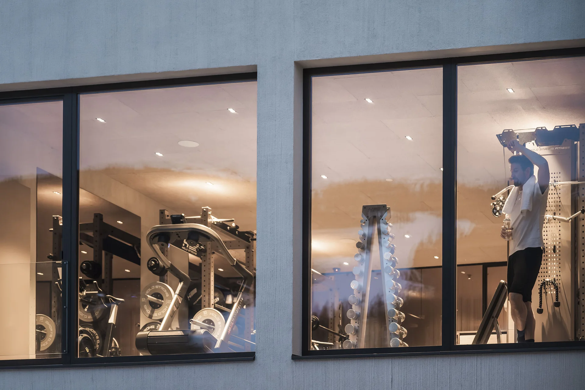 Fitness, Yoga, Outdoor-Erlebnisse: Aktivhotel in Südtirol Blick durch Fenster auf einen Mann im Fitnessstudio mit Gewichten.