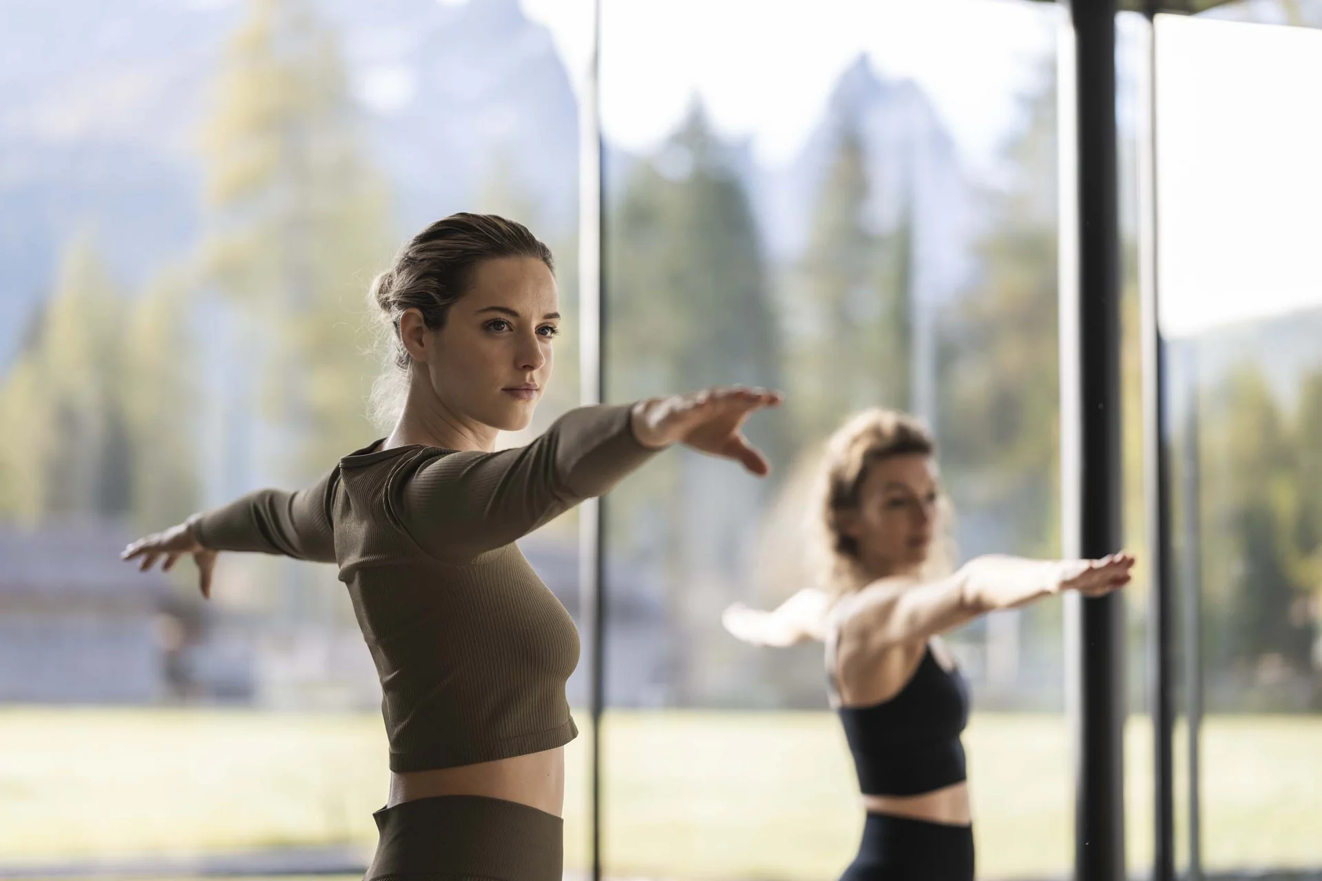 Hotel Monika in Sexten: Wohlbefinden inmitten der Dolomiten Zwei Frauen machen Yoga-Übung mit ausgestreckten Armen in hellem Raum