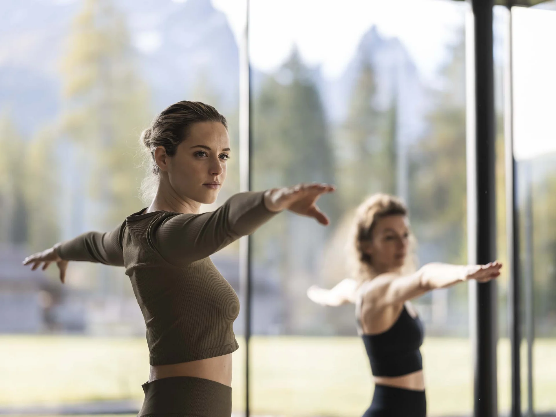 Fitness, yoga, outdoor fun: active hotel in South Tyrol. Two women doing yoga pose with arms extended in bright room