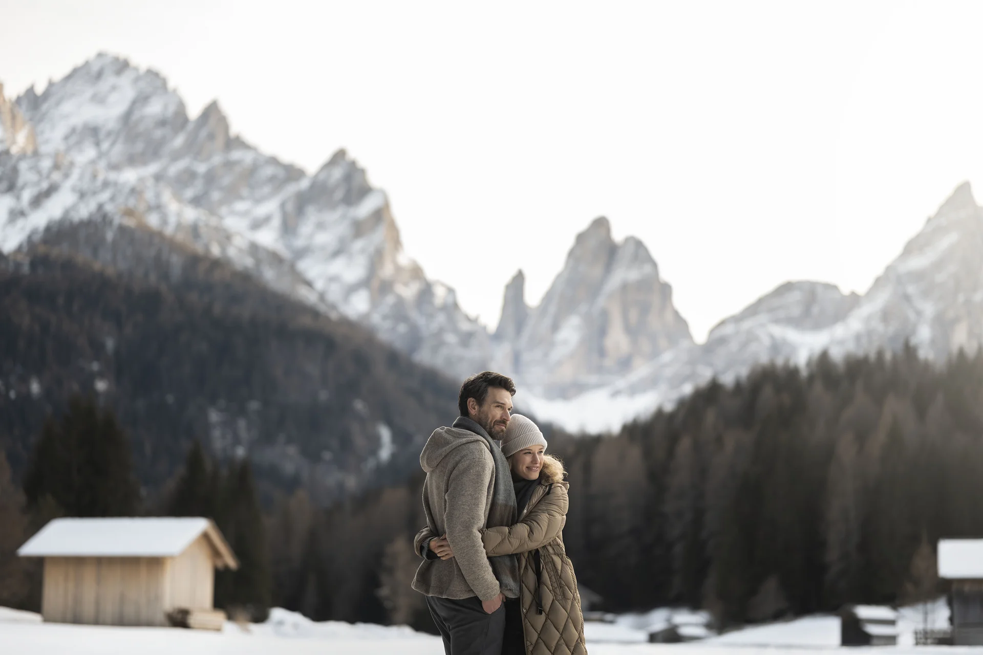 Hotel Monika in Sexten: Wohlbefinden inmitten der Dolomiten Paar umarmt sich im Schnee vor verschneiten Bergen und Hütten