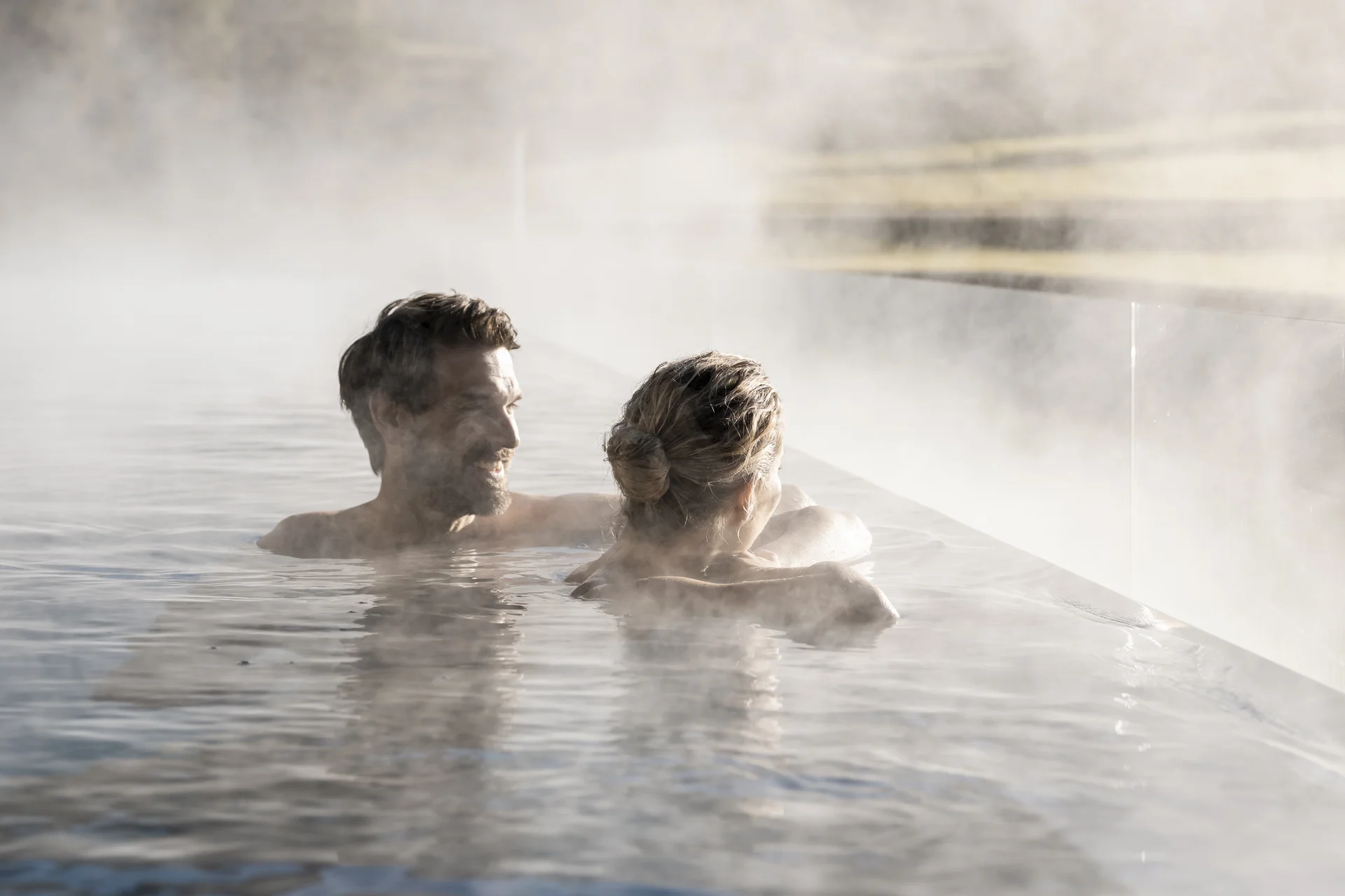 Hotel Monika in den Dolomiten – mit Pools und Spa Area Zwei Personen genießen einen beheizten Außenpool mit Dampf in der Berglandschaft
