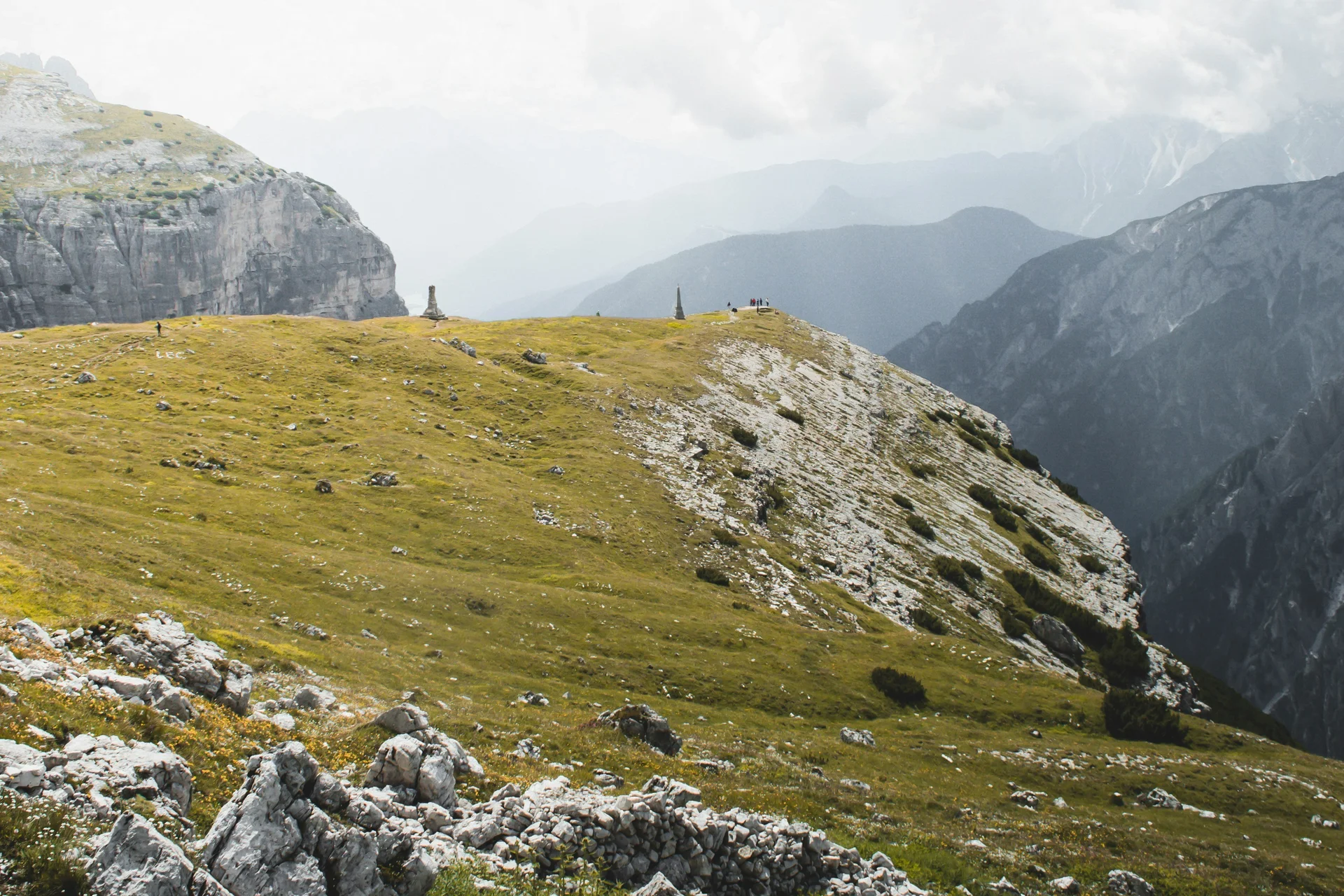 Sommer in den Bergen. In Ihrem Wanderhotel in den Dolomiten. Grüne Bergwiese mit Felsen und bewölktem Himmel in den Alpen